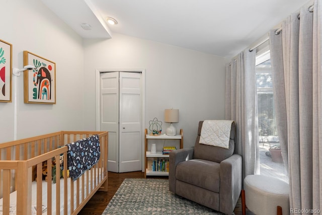 bedroom with vaulted ceiling, a crib, dark wood-style flooring, and a closet