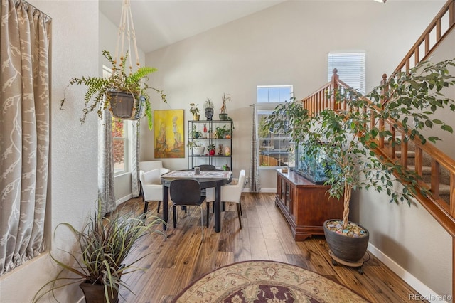 dining space with high vaulted ceiling, hardwood / wood-style floors, baseboards, and stairs