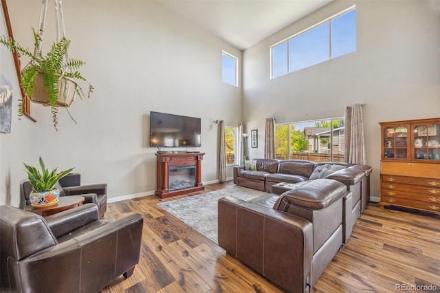 living room featuring a high ceiling, wood finished floors, a glass covered fireplace, and baseboards