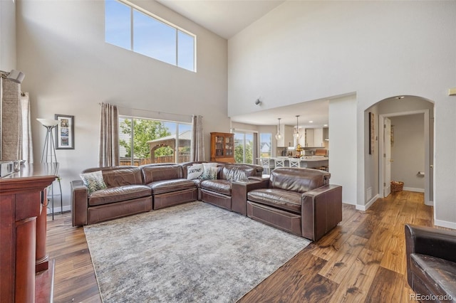 living area with wood finished floors, a towering ceiling, arched walkways, and baseboards