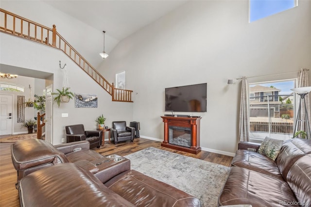 living area with high vaulted ceiling, a chandelier, wood finished floors, stairs, and baseboards