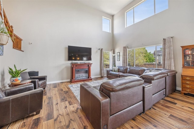 living room with a towering ceiling, wood finished floors, plenty of natural light, a glass covered fireplace, and baseboards