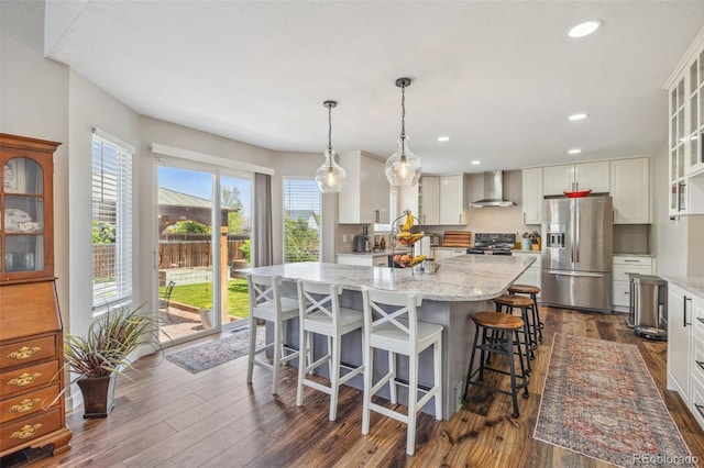 kitchen with stainless steel fridge, wall chimney range hood, stove, dark wood finished floors, and glass insert cabinets
