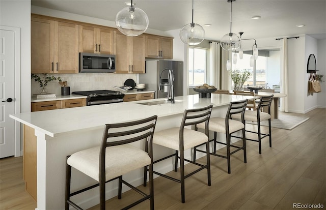 21166 E 62nd Dr, Aurora, CO 80019 - kitchen featuring appliances with stainless steel finishes, light countertops, decorative backsplash, light wood-style flooring, and a center island with sink