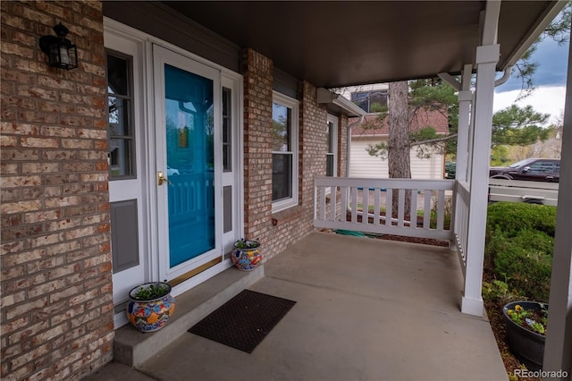 view of exterior entry featuring brick siding and covered porch