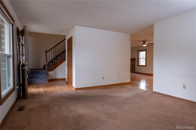 spare room with carpet floors, ceiling fan, visible vents, and stairs