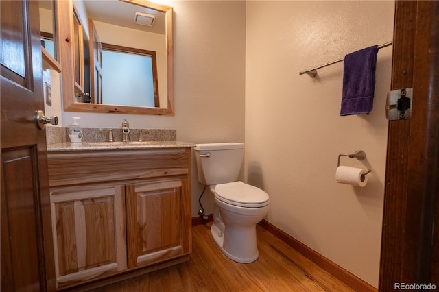 bathroom featuring baseboards, wood finished floors, toilet, and vanity