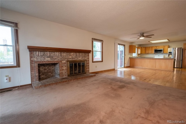 unfurnished living room with a brick fireplace, baseboards, light colored carpet, a textured ceiling, and a ceiling fan