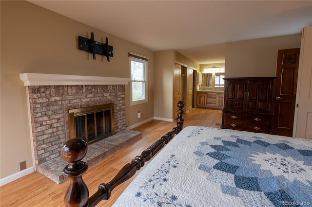 bedroom with a brick fireplace, baseboards, wood finished floors, and ensuite bathroom