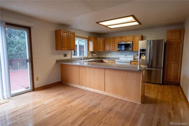kitchen featuring a peninsula, appliances with stainless steel finishes, a healthy amount of sunlight, and light wood finished floors