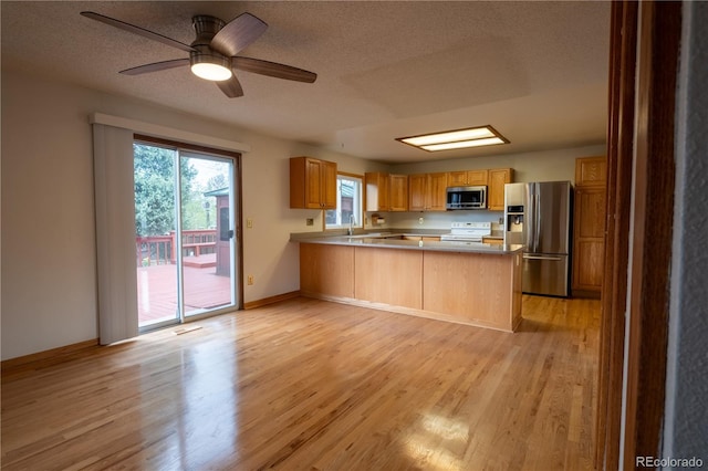 kitchen with a peninsula, light wood-style flooring, appliances with stainless steel finishes, and a textured ceiling