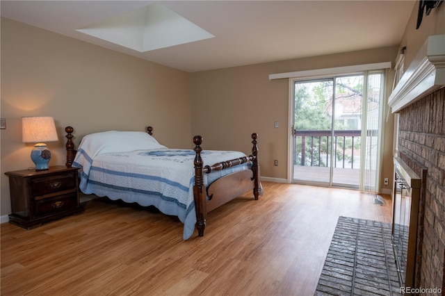 bedroom featuring a skylight, a fireplace, baseboards, light wood-style floors, and access to outside