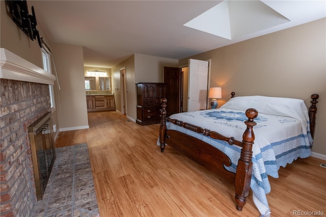 bedroom featuring baseboards, a skylight, wood finished floors, and a fireplace