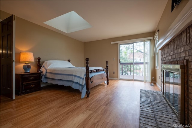 bedroom with a skylight, a brick fireplace, baseboards, access to outside, and light wood-style flooring