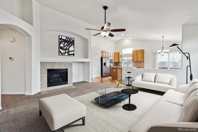 living room featuring light carpet, high vaulted ceiling, ceiling fan with notable chandelier, and a tile fireplace