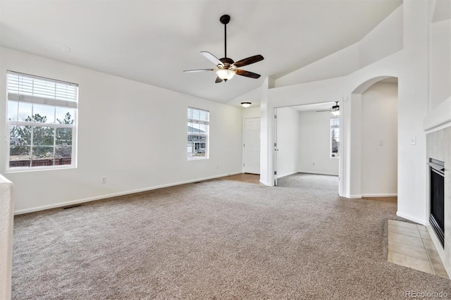 unfurnished living room with light carpet, arched walkways, a tiled fireplace, lofted ceiling, and ceiling fan