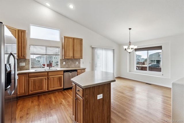 kitchen featuring stainless steel appliances, a sink, light wood-style floors, brown cabinets, and a center island