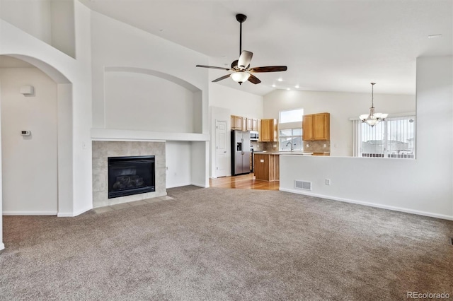 unfurnished living room featuring light colored carpet, visible vents, a tiled fireplace, a sink, and ceiling fan with notable chandelier