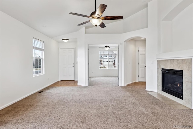 unfurnished living room featuring baseboards, arched walkways, a tile fireplace, ceiling fan, and carpet