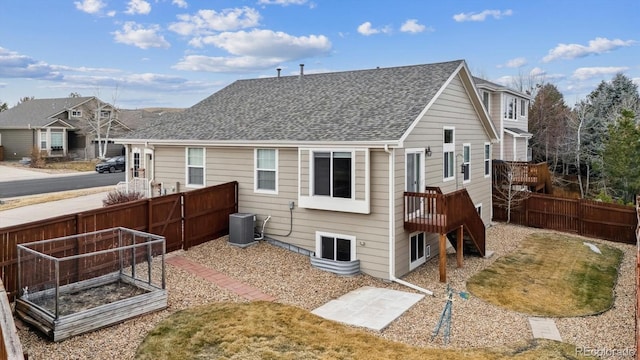 rear view of property with central AC, roof with shingles, a vegetable garden, and fence