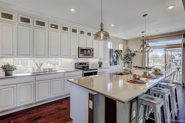 kitchen featuring white cabinetry, stainless steel appliances, an island with sink, sink, and hanging light fixtures