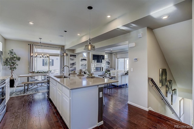 kitchen with pendant lighting, a center island with sink, sink, white cabinetry, and dark hardwood / wood-style flooring