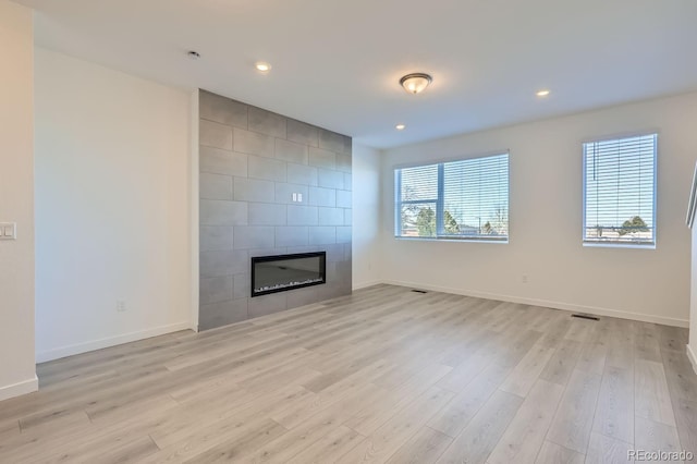 unfurnished living room with a tiled fireplace and light wood-type flooring