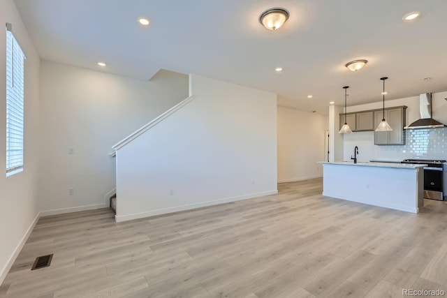 kitchen featuring tasteful backsplash, gray cabinetry, stainless steel range with electric cooktop, an island with sink, and wall chimney exhaust hood