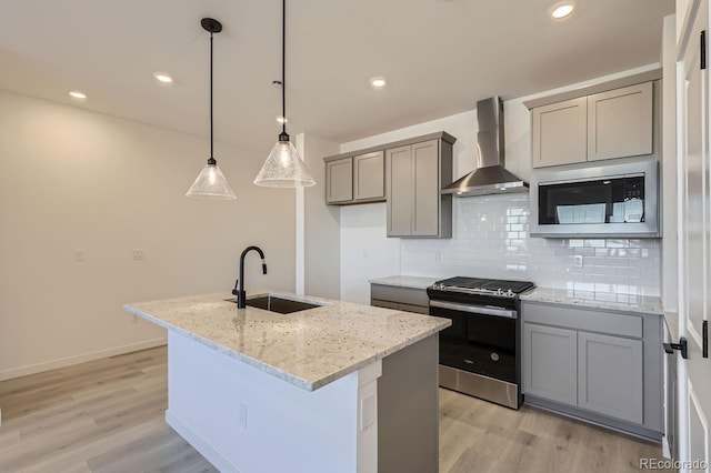 kitchen with wall chimney range hood, decorative light fixtures, sink, a center island with sink, and stainless steel range with gas cooktop