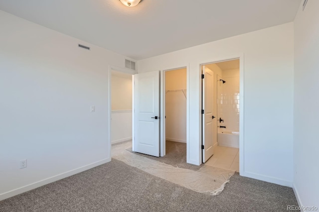 unfurnished bedroom with ensuite bath, light carpet, a closet, and a walk in closet