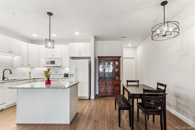 kitchen with pendant lighting, sink, white appliances, a center island, and white cabinets