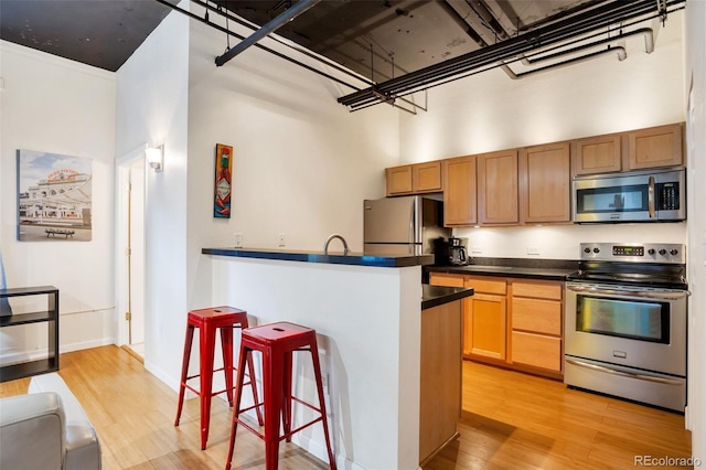 kitchen featuring a breakfast bar, a towering ceiling, stainless steel appliances, and light hardwood / wood-style flooring