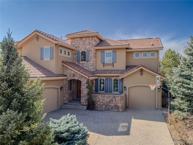 mediterranean / spanish house featuring a garage, concrete driveway, stone siding, a tile roof, and stucco siding