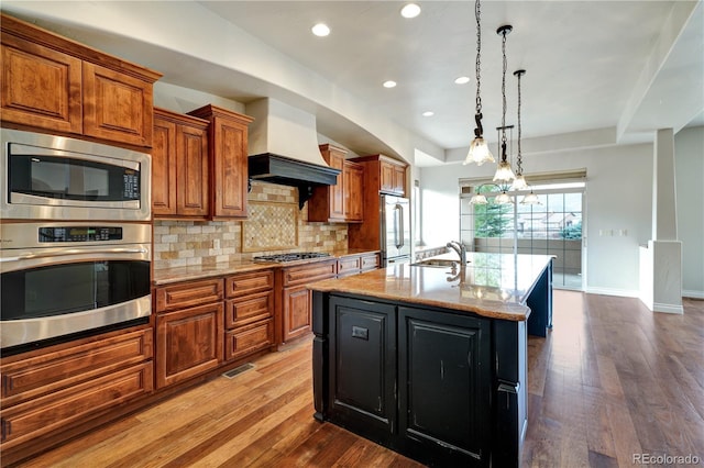 kitchen featuring brown cabinets, backsplash, appliances with stainless steel finishes, a sink, and hardwood / wood-style flooring