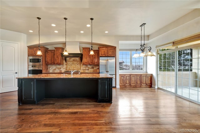 kitchen featuring custom range hood, brown cabinets, dark wood-style flooring, built in appliances, and backsplash