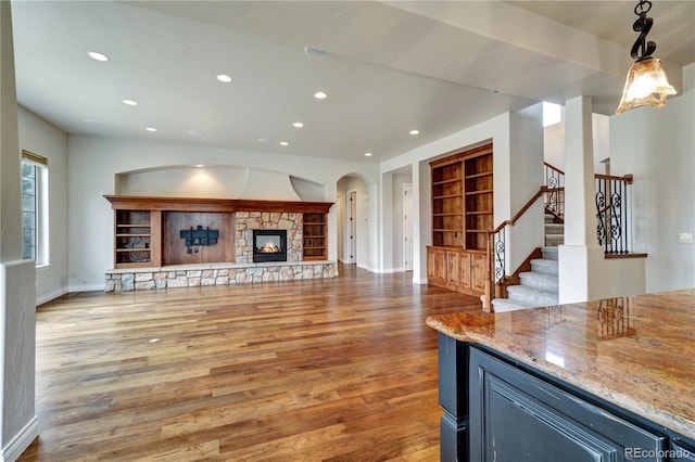 unfurnished living room with a stone fireplace, stairway, wood finished floors, and recessed lighting