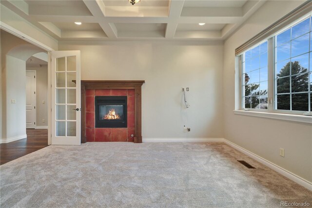 unfurnished living room featuring arched walkways, carpet, a tiled fireplace, and baseboards