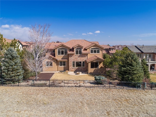 view of front of house with stone siding, a tile roof, a patio area, and fence