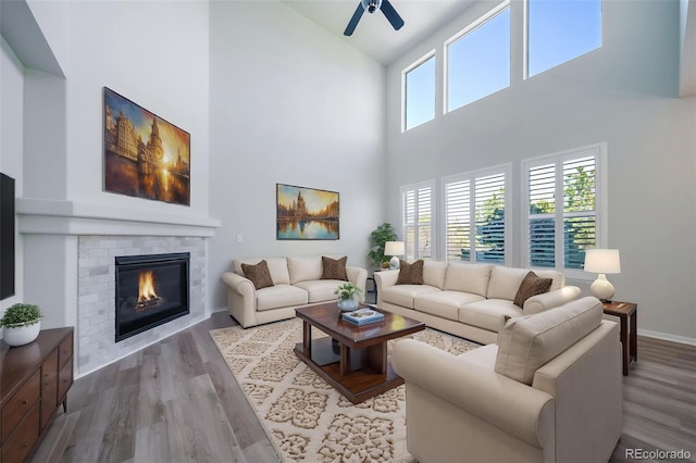 living room featuring a glass covered fireplace, wood finished floors, baseboards, high vaulted ceiling, and a ceiling fan