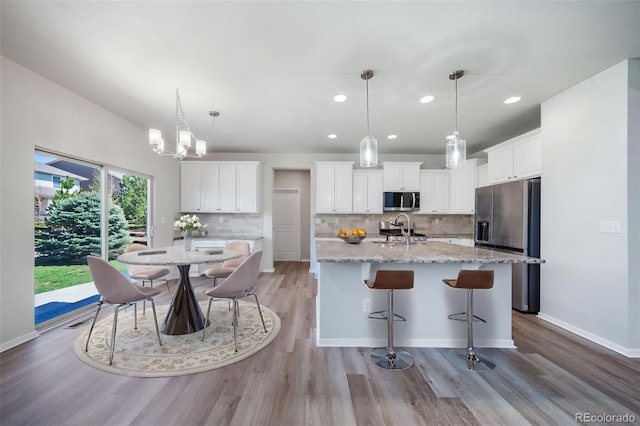 kitchen featuring a center island with sink, backsplash, stainless steel appliances, and light wood-type flooring