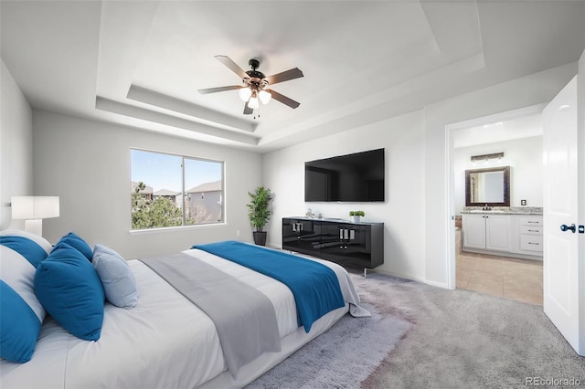 bedroom featuring a sink, baseboards, connected bathroom, light carpet, and a tray ceiling