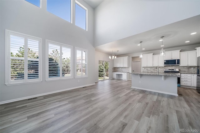 unfurnished living room with visible vents, an inviting chandelier, light wood-style floors, a high ceiling, and recessed lighting