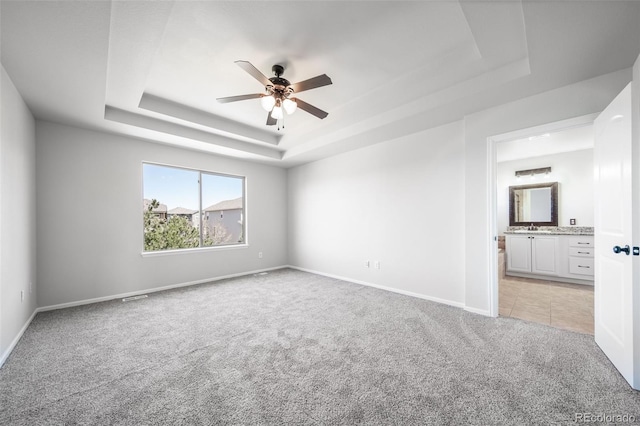 unfurnished room with ceiling fan, a sink, a raised ceiling, baseboards, and light carpet