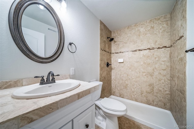 bathroom featuring toilet, tiled shower, and vanity
