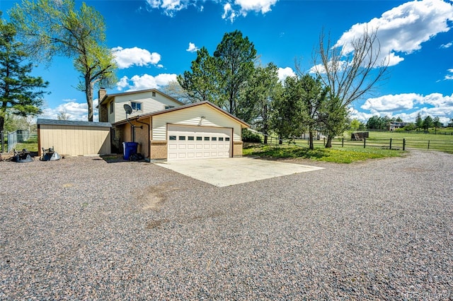 view of side of property with gravel driveway, an attached garage, fence, a chimney, and brick siding
