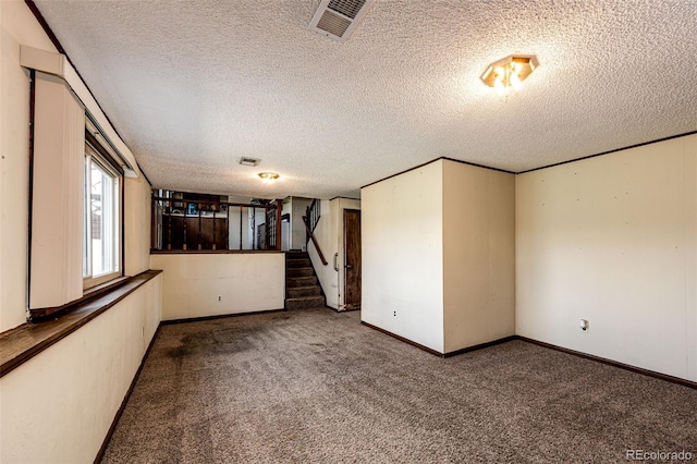 carpeted empty room with a textured ceiling, stairs, and baseboards