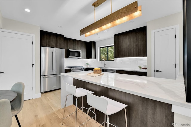 2164 S Ash St, Denver, CO 80222 - kitchen featuring stainless steel appliances, a kitchen bar, decorative backsplash, light wood-type flooring, and dark brown cabinetry
