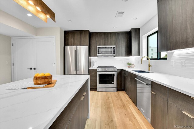 2164 S Ash St, Denver, CO 80222 - kitchen with stainless steel appliances, a sink, light wood-style flooring, decorative backsplash, and dark brown cabinets