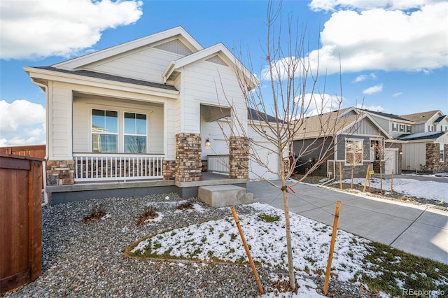 craftsman inspired home with fence, driveway, covered porch, stone siding, and a garage