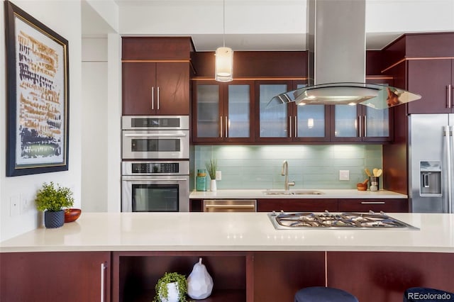 kitchen with pendant lighting, sink, island range hood, backsplash, and appliances with stainless steel finishes